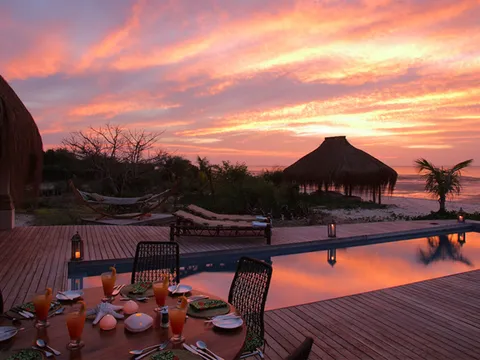 Table set on a deck by a pool at sunset, next to a beach