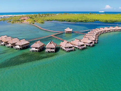 Aerial view of thatched bungalows over the water in a turquoise lagoon