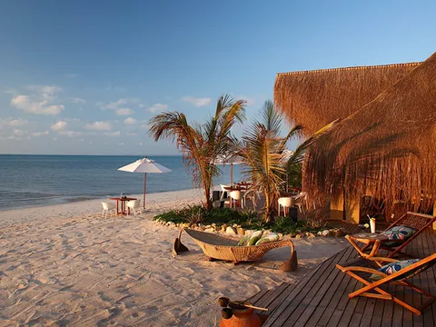 Terrace of a thatched beach lodge with loungers on the sand